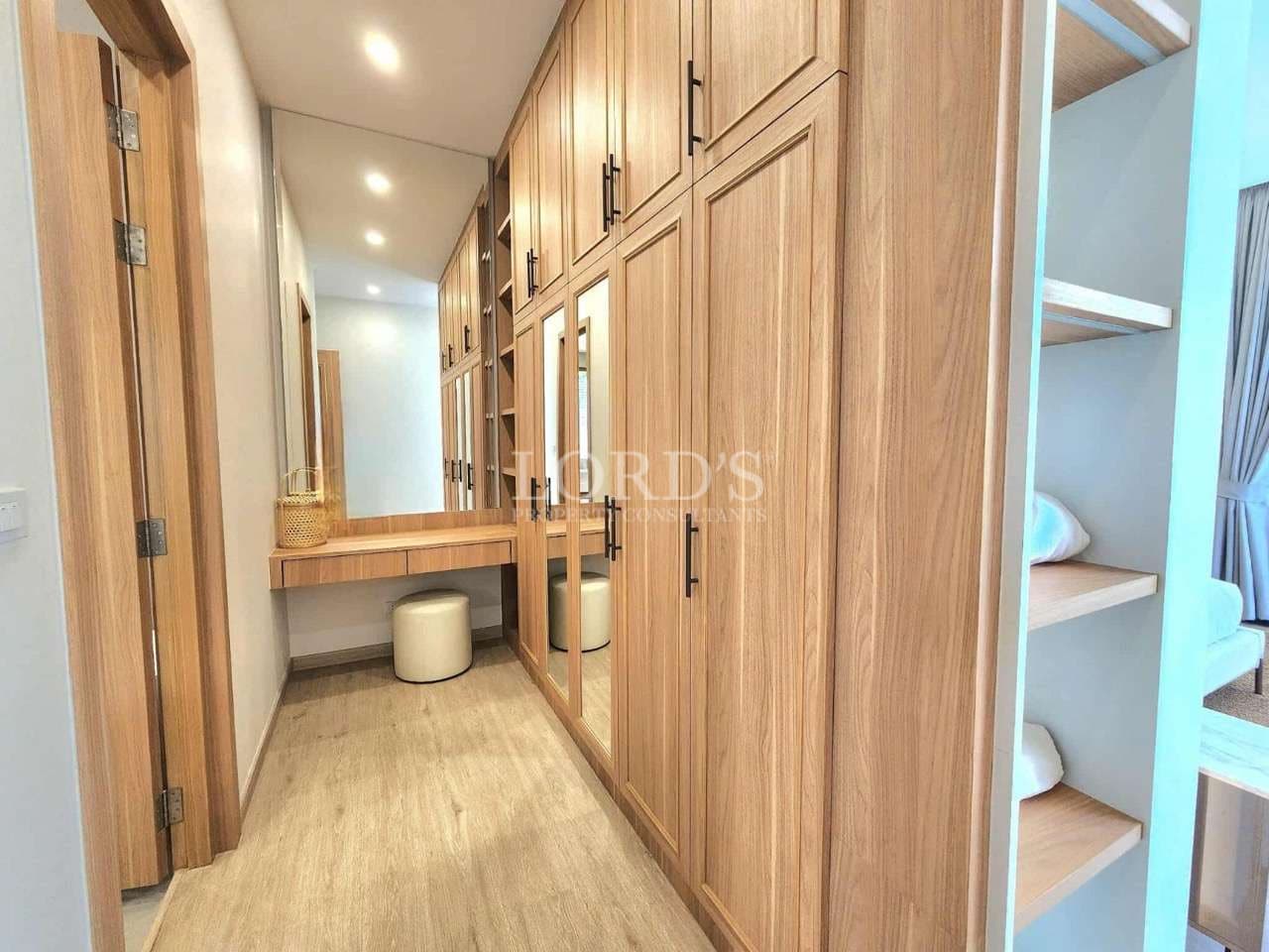 Walk-in wooden wardrobe with built-in cabinets, mirrored doors, vanity desk, and modern lighting