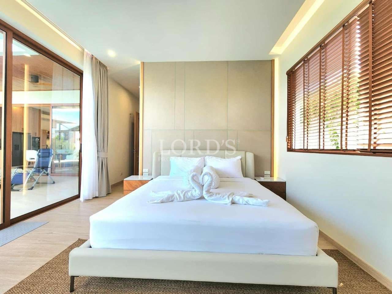 Bright modern bedroom with king-size bed, sliding glass doors, wooden blinds, and poolside view