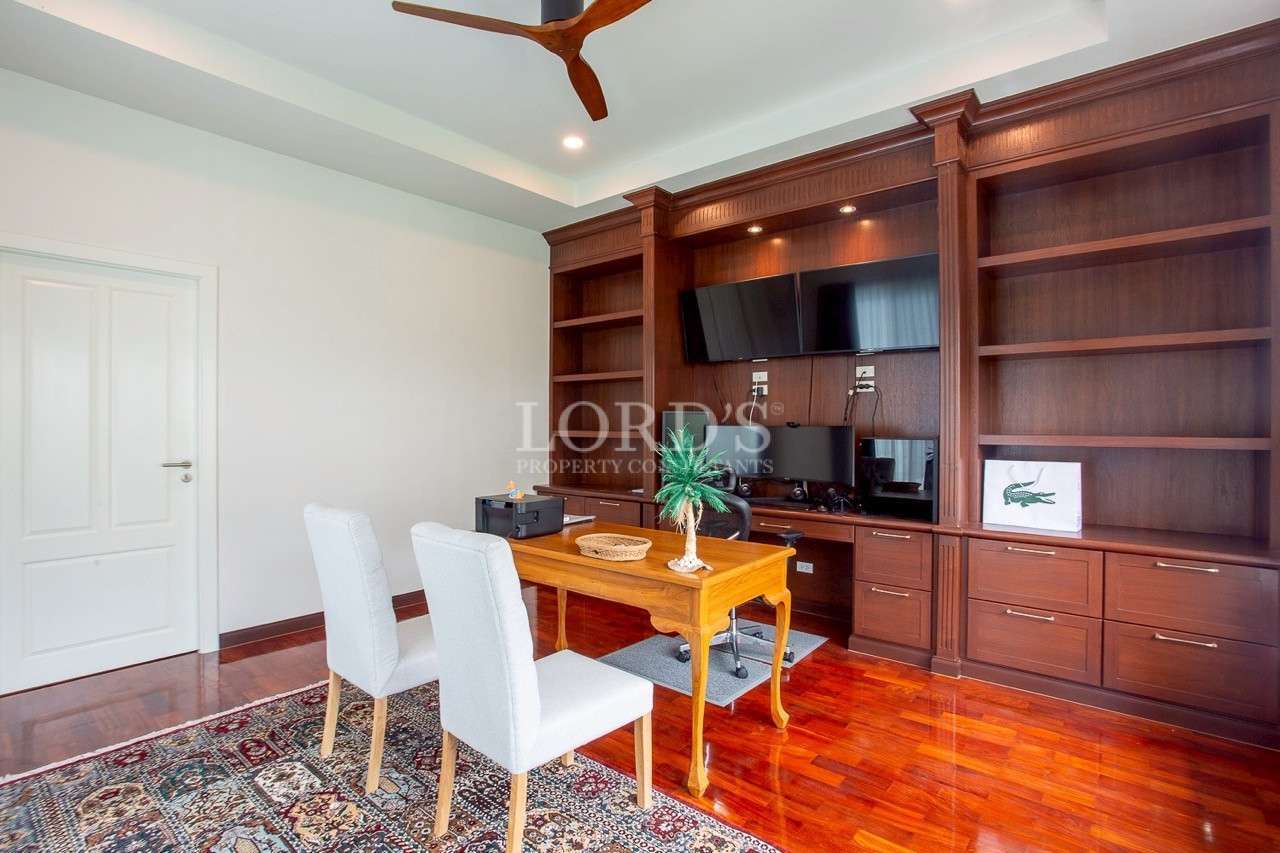 Home office with large wooden built-in shelving unit, desk, upholstered chairs, and polished wood flooring.