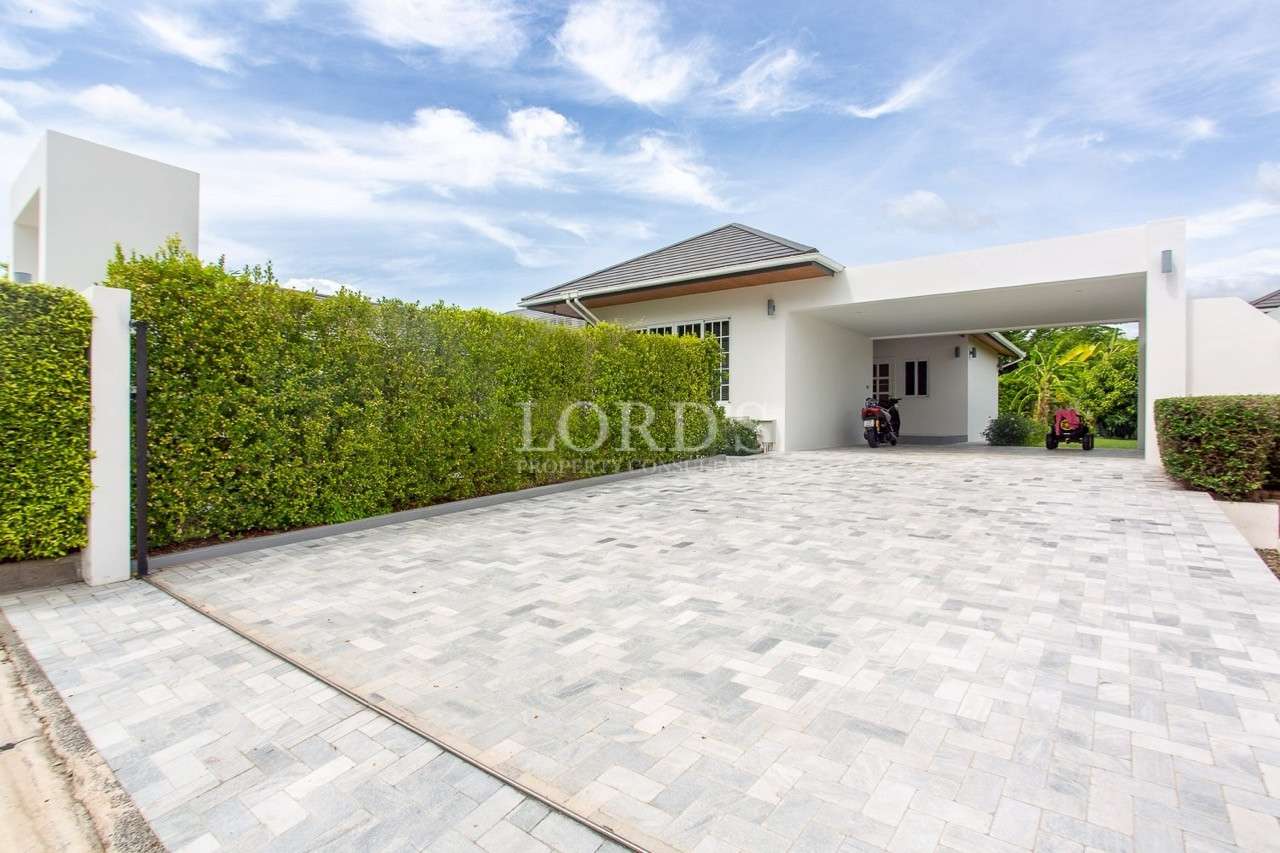 Spacious paved driveway with covered carport and trimmed hedge wall.