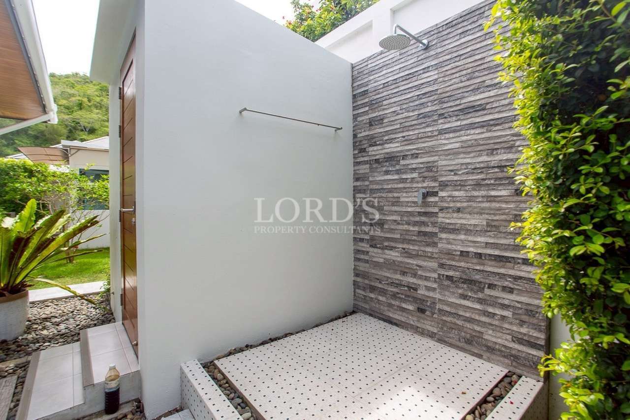 Modern outdoor shower area with stone accent wall and rain shower head.