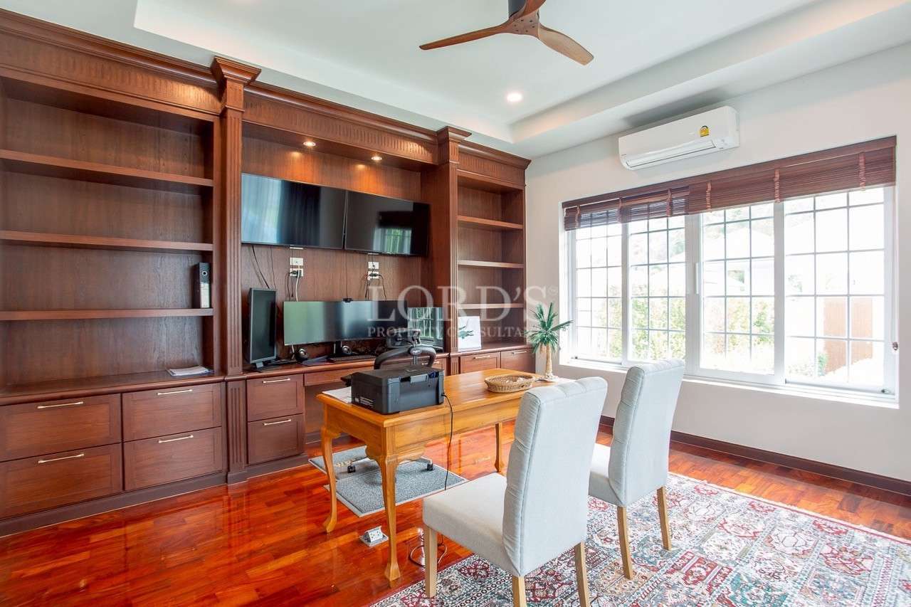 Bright home office with wooden built-in shelves, desk with printer, dual monitors, and large window.