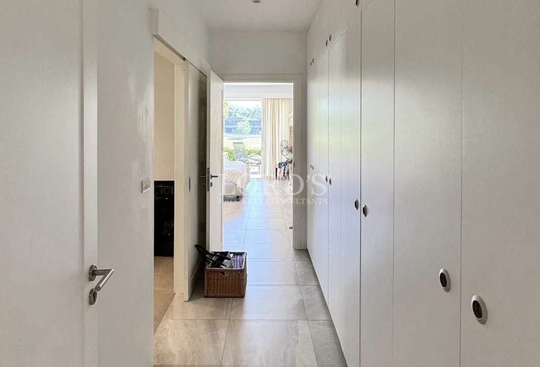 Bright hallway with white built-in wardrobes leading to a bedroom with large windows and garden view.