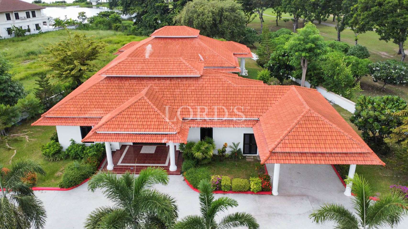 Oblique aerial view of a single-story white house with a terracotta-tiled roof, covered carport, and landscaped yard.