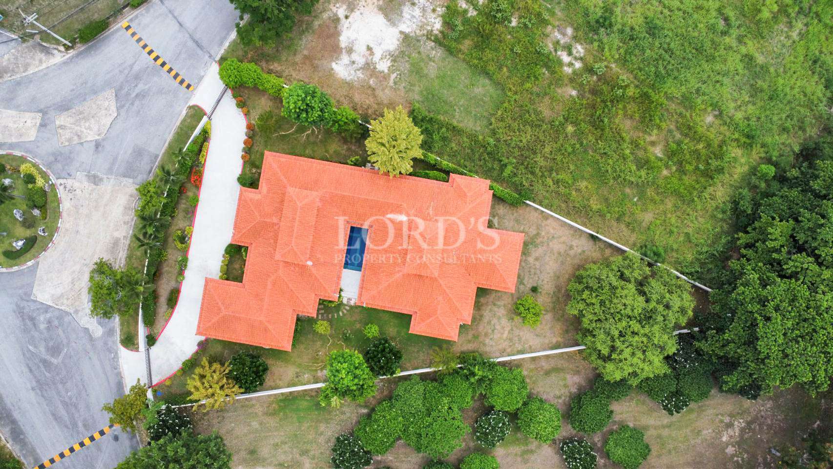 Aerial view of a large house with a red-tiled roof surrounded by trees and greenery.