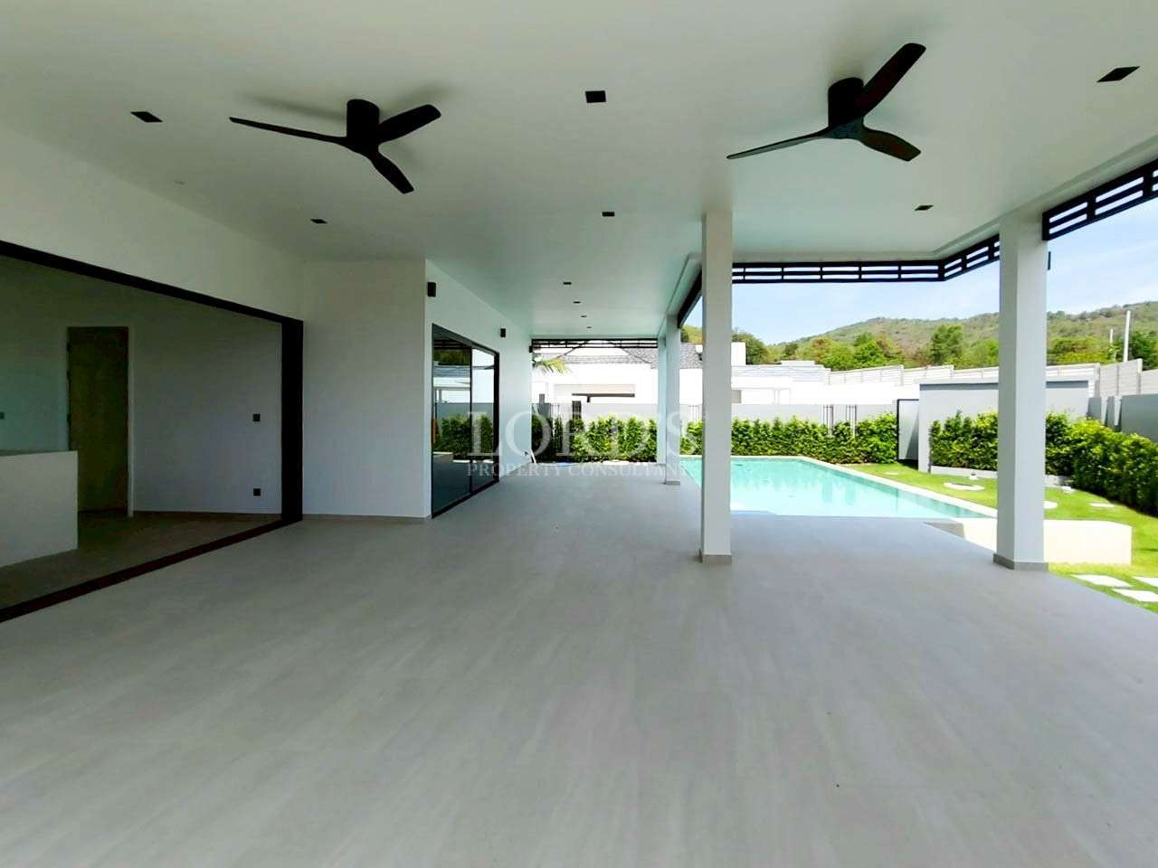 Covered outdoor terrace with ceiling fans overlooking a private swimming pool and garden.