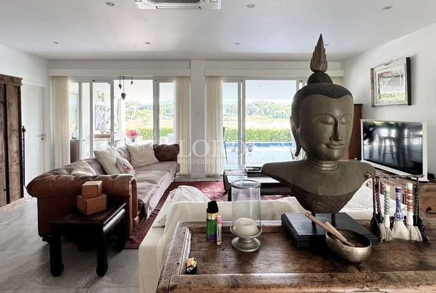 Bright living room with large Buddha sculpture, sofa seating, and sliding doors overlooking outdoor greenery.