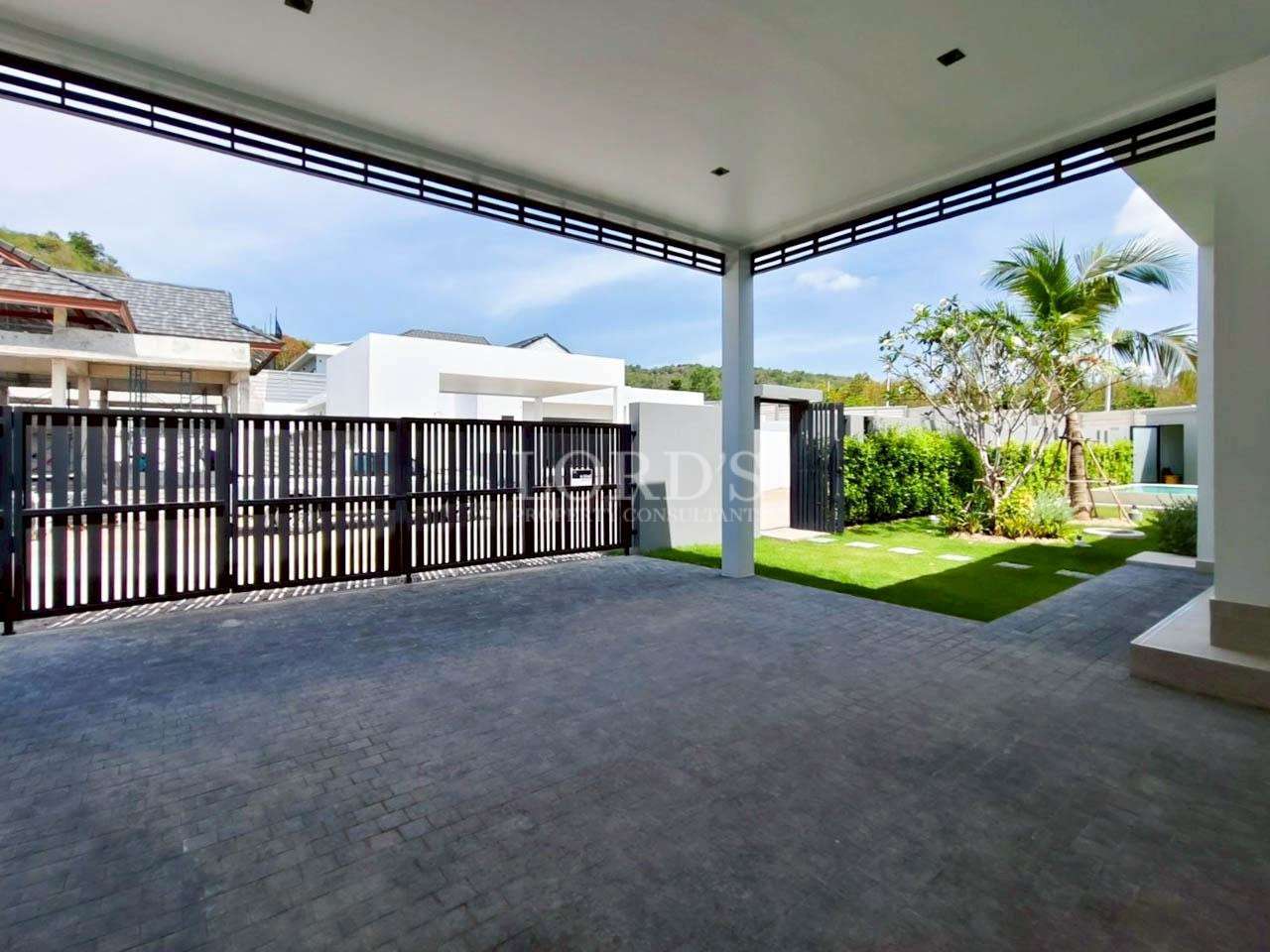 Covered carport with tiled driveway, sliding gate, and landscaped garden with palm tree.
