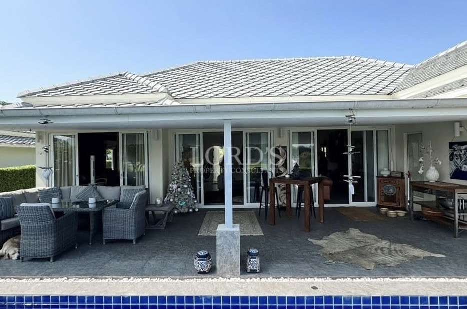 Covered patio of a single-story home with outdoor seating, sliding glass doors, and pool edge in the foreground.
