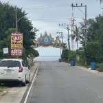Quiet roadside street leading toward the sea with Thai signage and decorative archway.