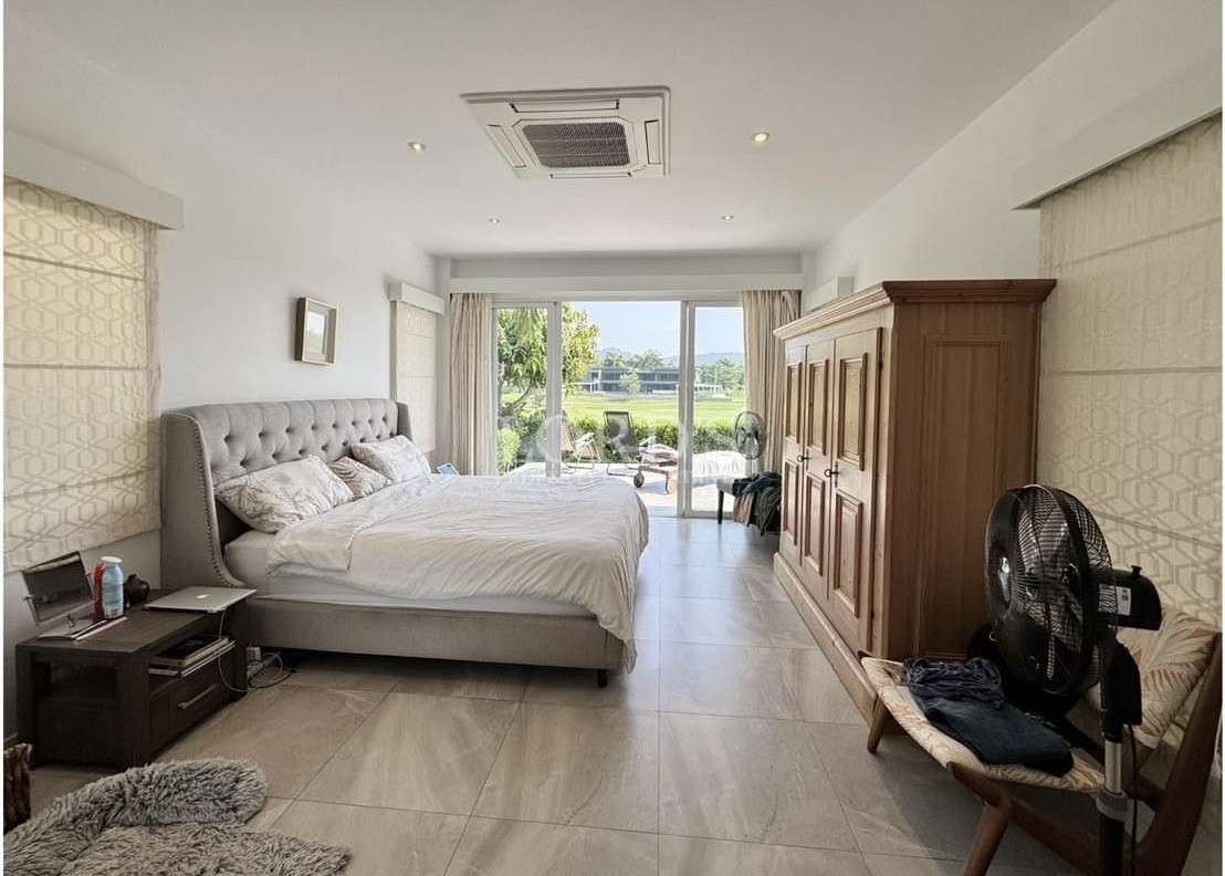 Bright bedroom with upholstered bed, wooden wardrobe, tiled floor, and sliding glass doors opening to a patio with greenery views.