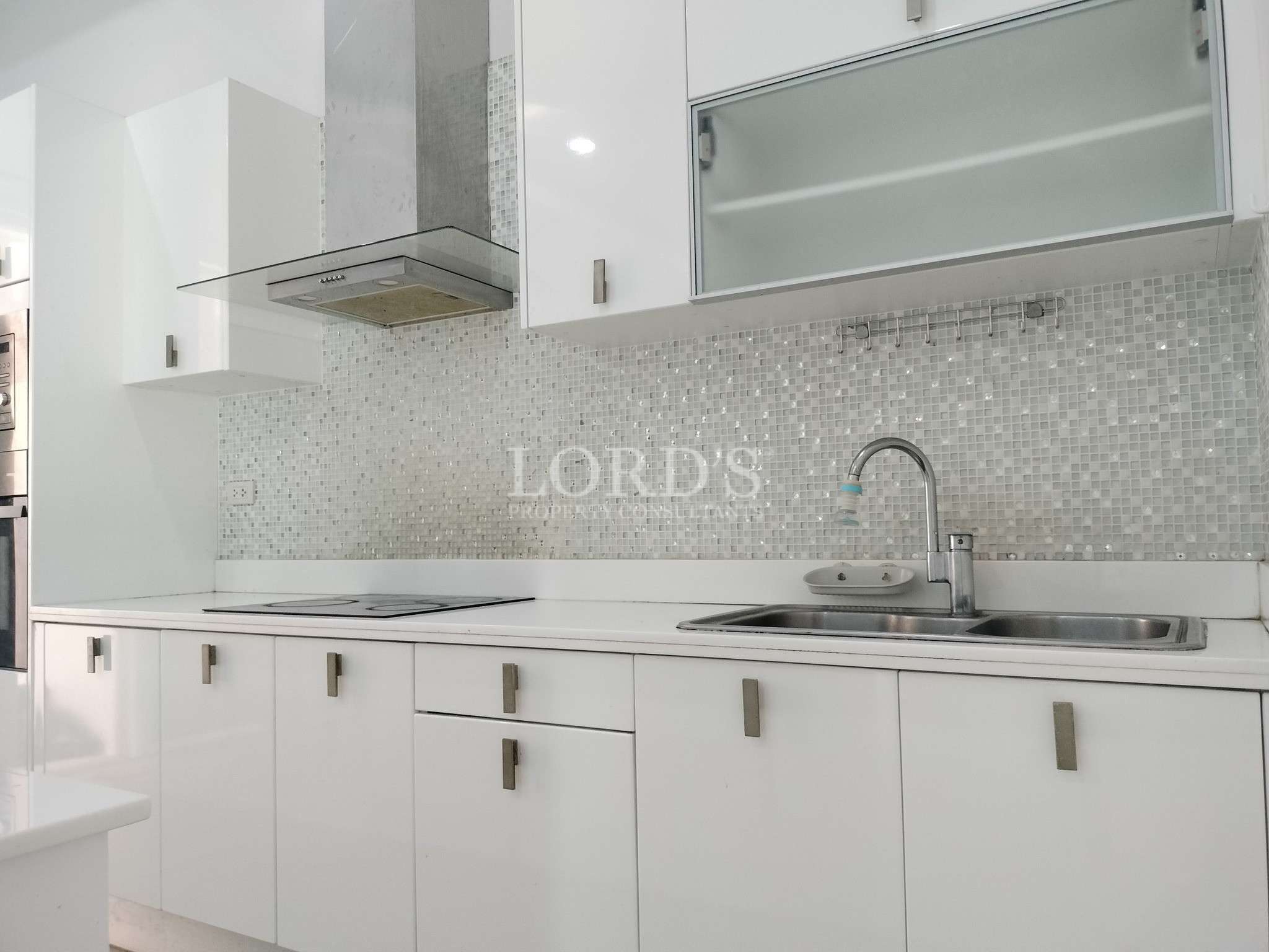 Modern white kitchen with mosaic tile backsplash, stainless steel range hood, and double sink.