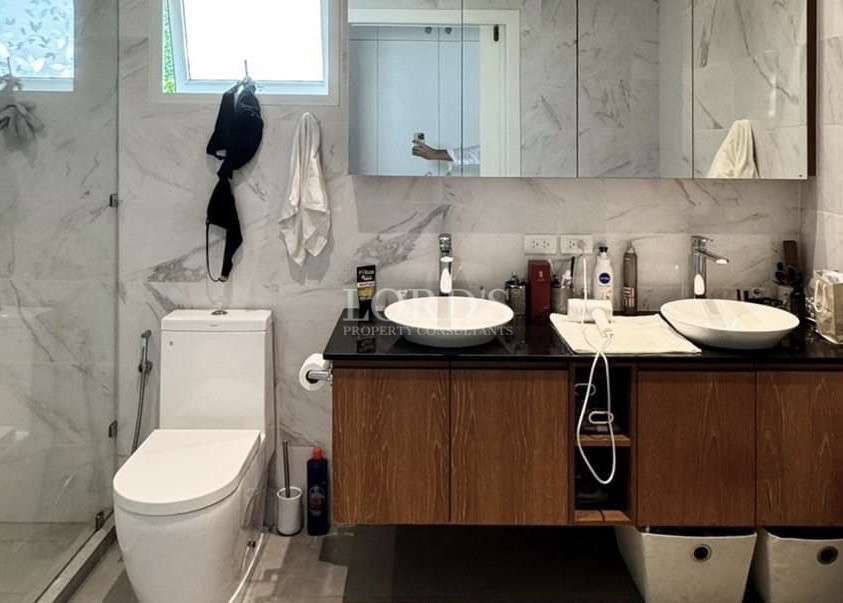 Modern bathroom with marble walls, glass shower enclosure, double vessel sinks on a wooden vanity, and a large mirror.