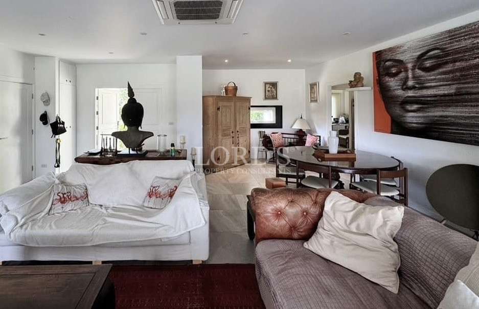 Cozy open-plan living and dining area with sofas, wooden furniture, decorative Buddha statue, and large portrait artwork on the wall.