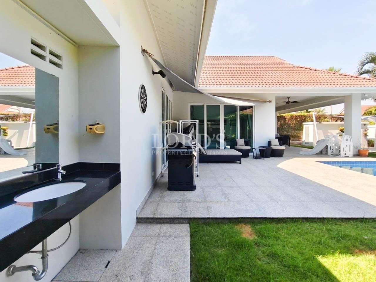 Covered outdoor patio with grill beside luxury villa