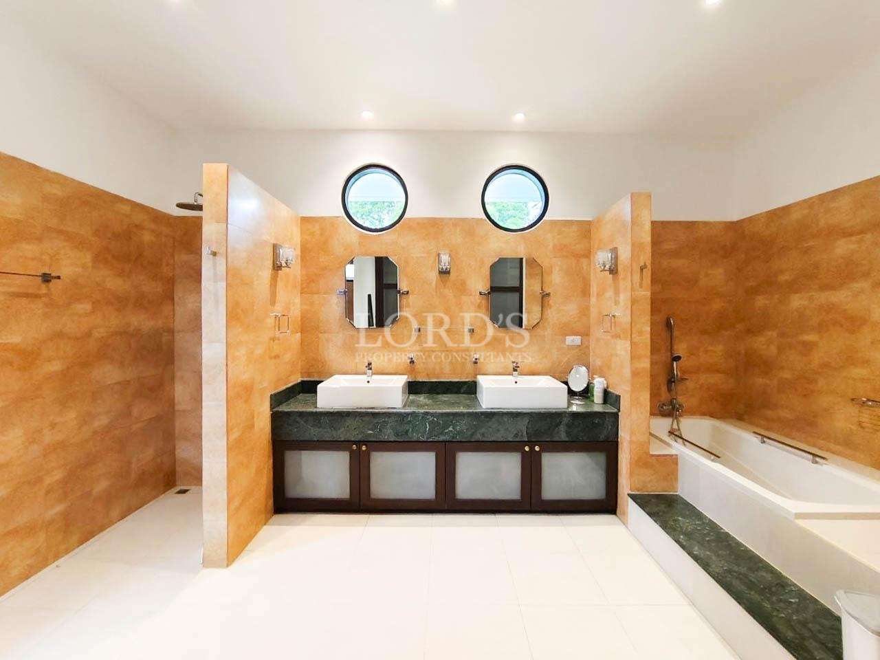 Luxury bathroom with double sinks, walk-in showers, bathtub, and round windows