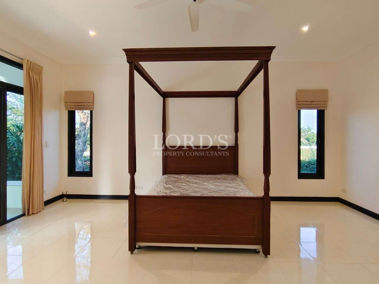Spacious bedroom with wooden four-poster bed, glossy tiled floor, and tall narrow windows with garden views.