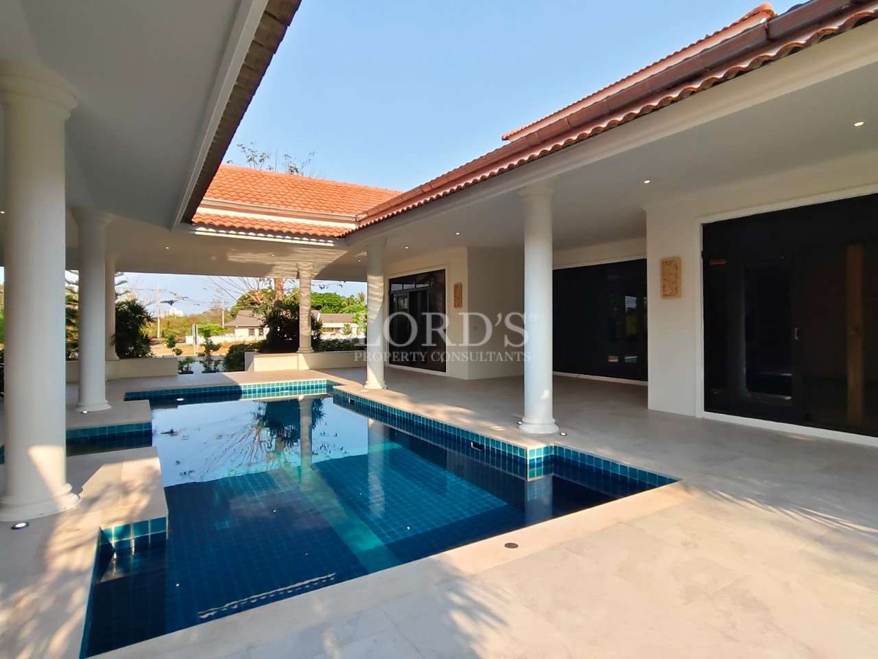 Private villa courtyard with covered patio, white columns, red tile roof, and blue tiled swimming pool.