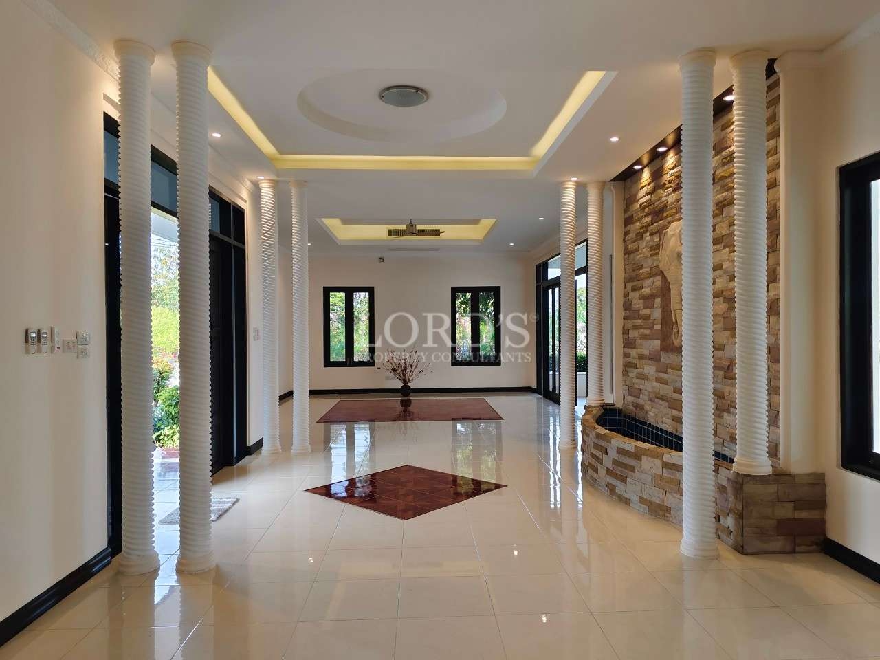 Spacious luxury foyer with white columns, glossy tiled floor, recessed ceiling lighting, and stone accent wall.