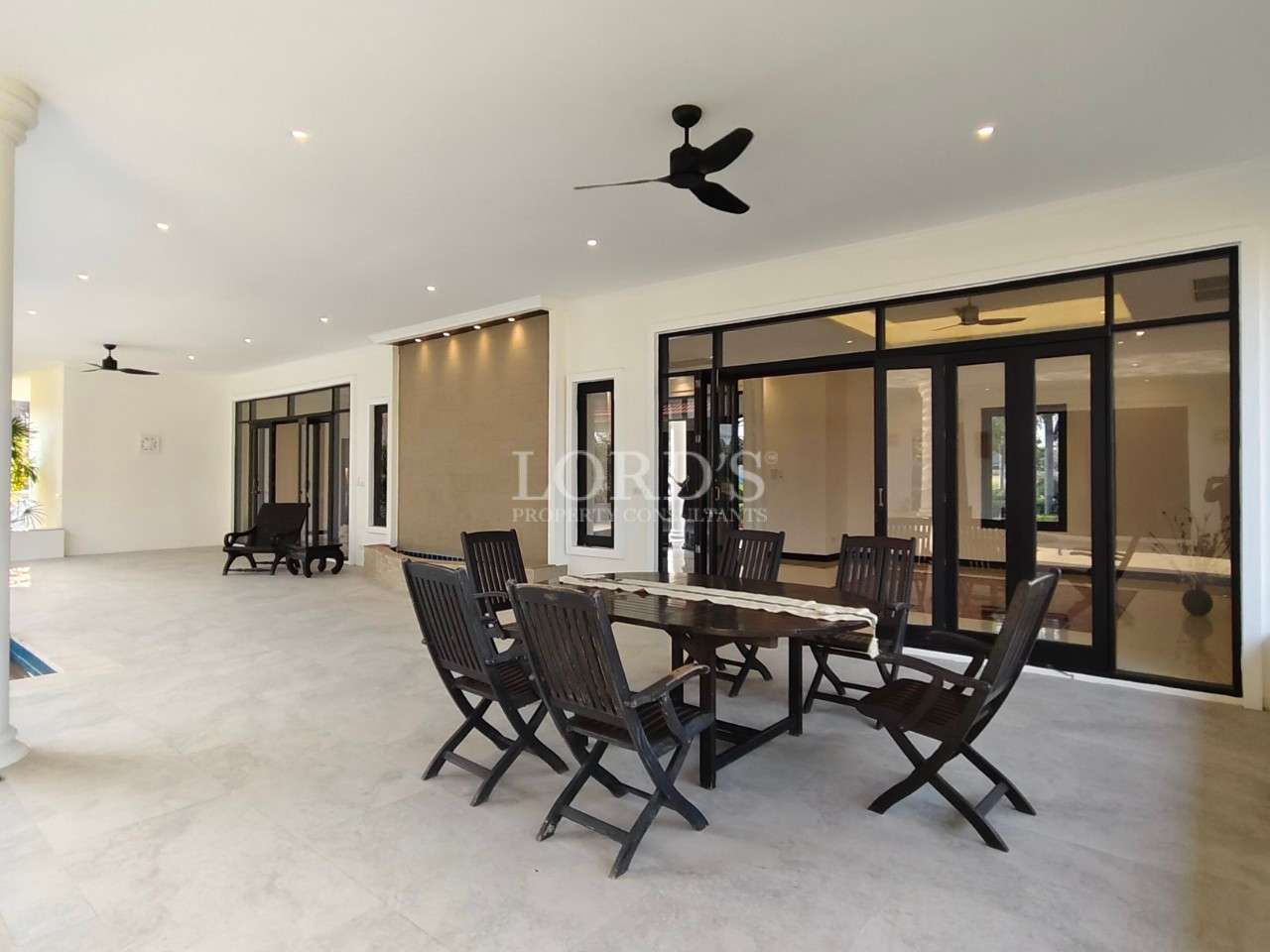 Covered outdoor patio with wooden dining table and chairs, ceiling fan, and large sliding glass doors leading indoors.