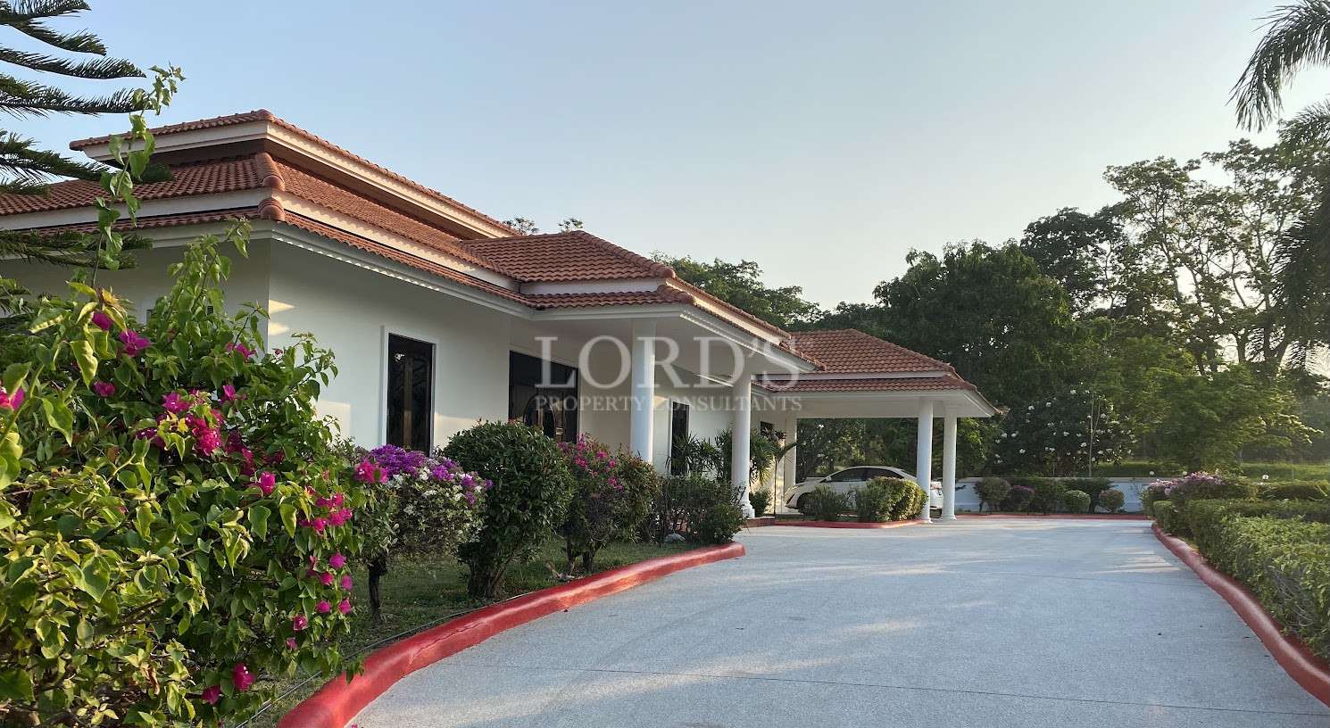 Luxury single-story villa with red tiled roof, landscaped garden, and curved driveway leading to a covered carport.