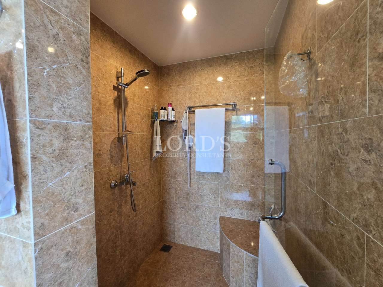 Modern walk-in shower with glass partition, rainfall showerhead, and brown marble-style tiled walls.