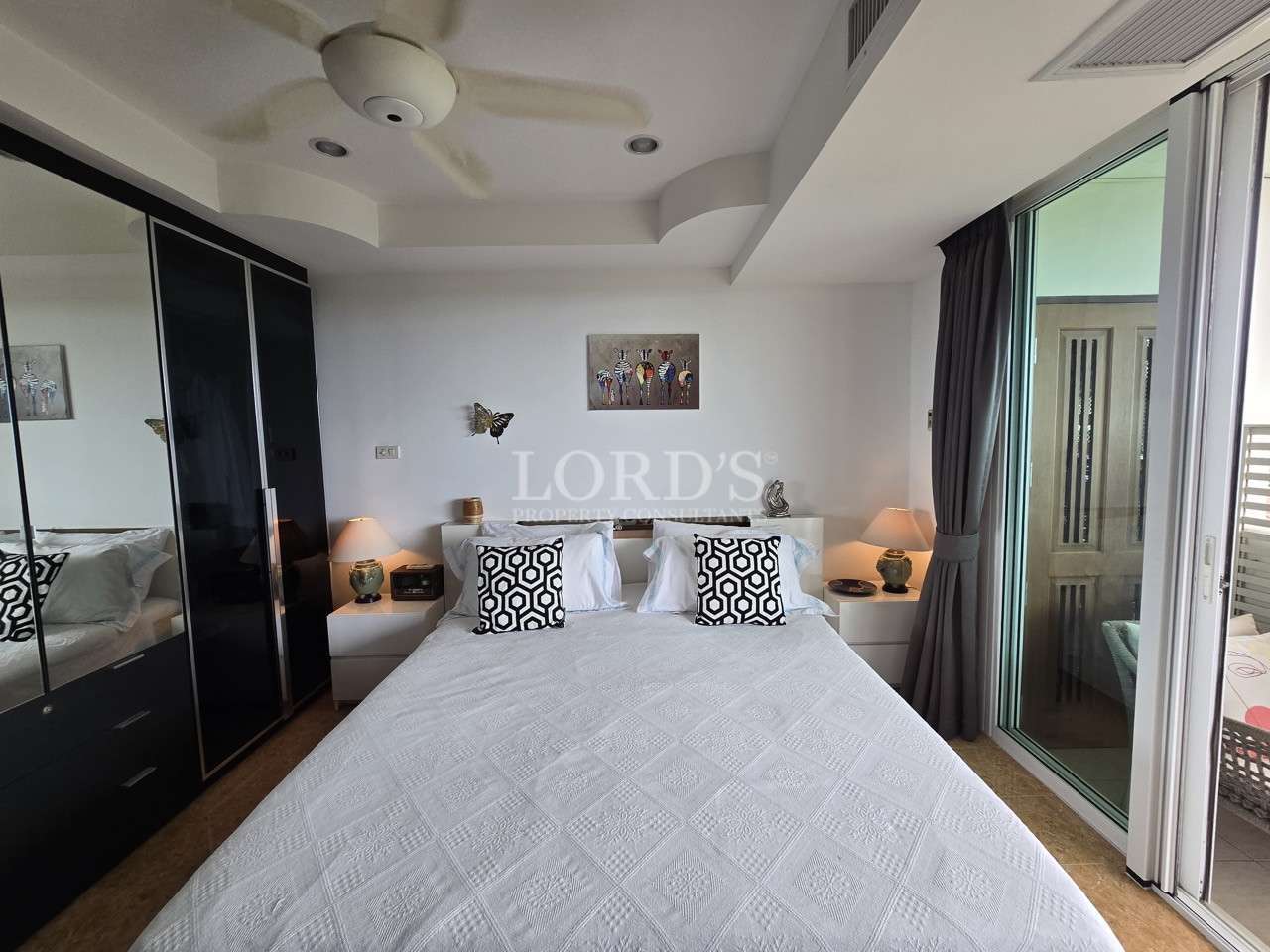 Bright modern bedroom with a double bed, bedside lamps, built-in wardrobe, and sliding glass doors leading to a balcony.