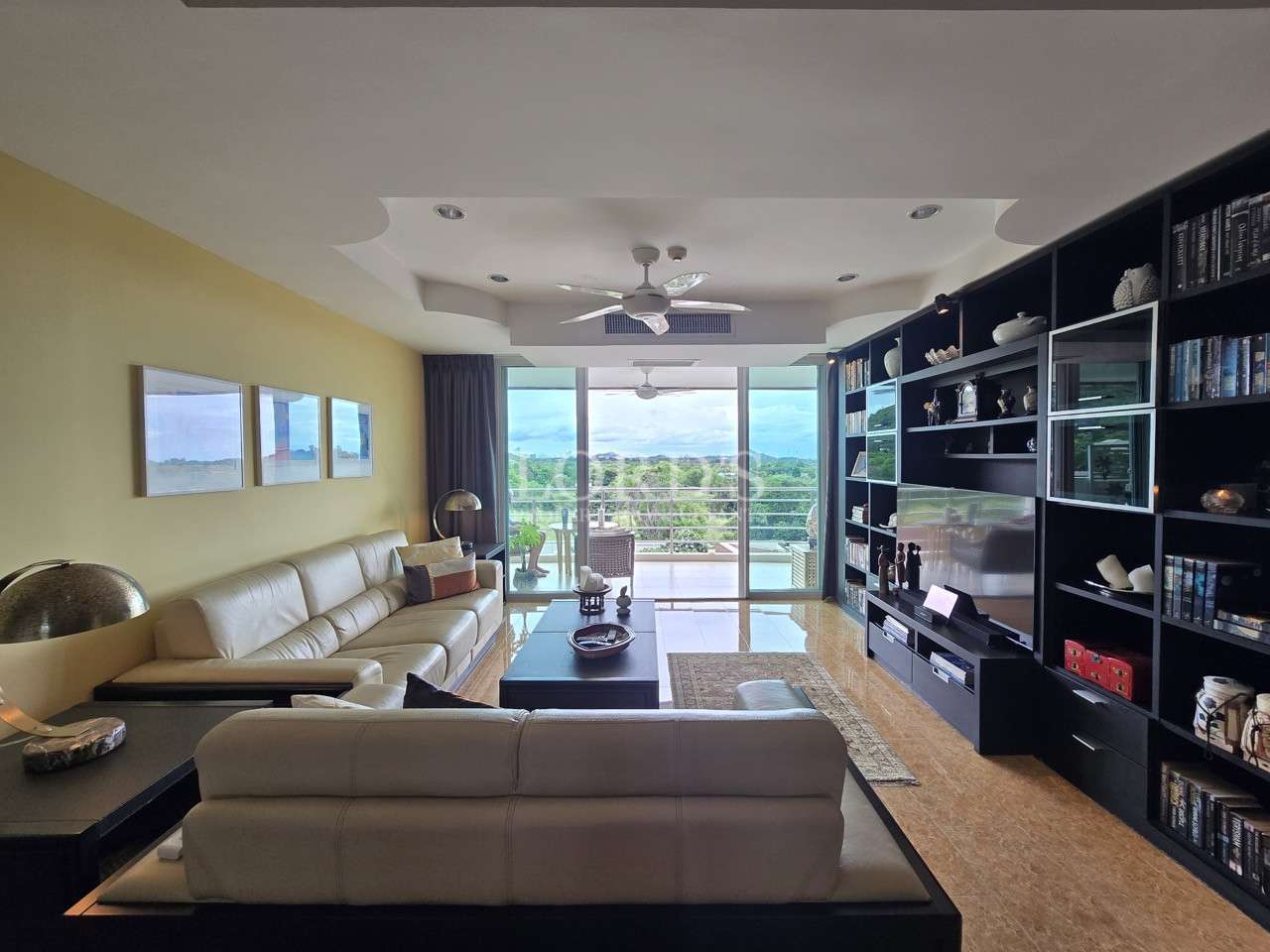 Modern living room with leather sofas, built-in shelving, and balcony views through large glass doors.