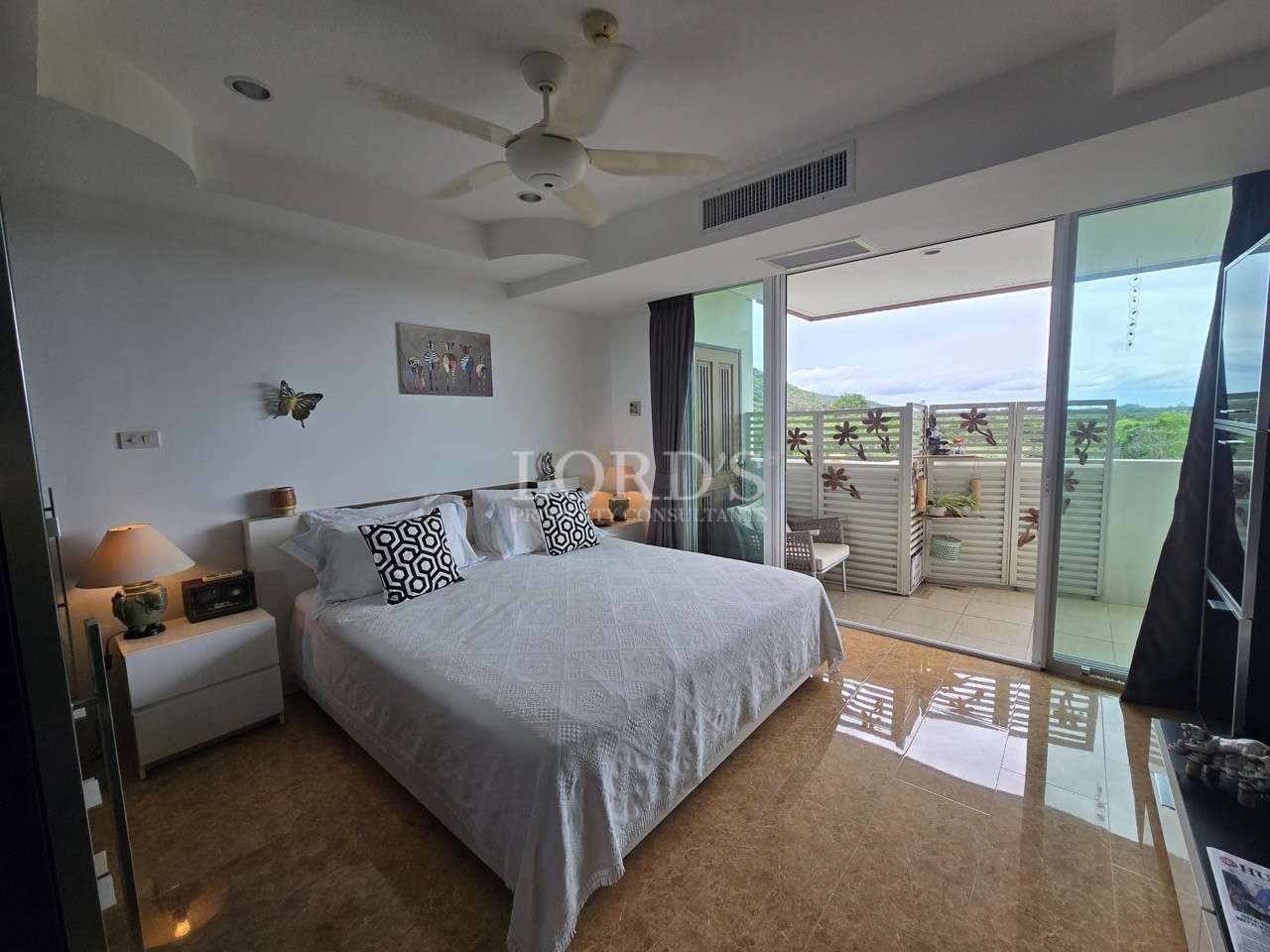 Bright bedroom with large bed, ceiling fan, and sliding glass doors opening to a private balcony.
