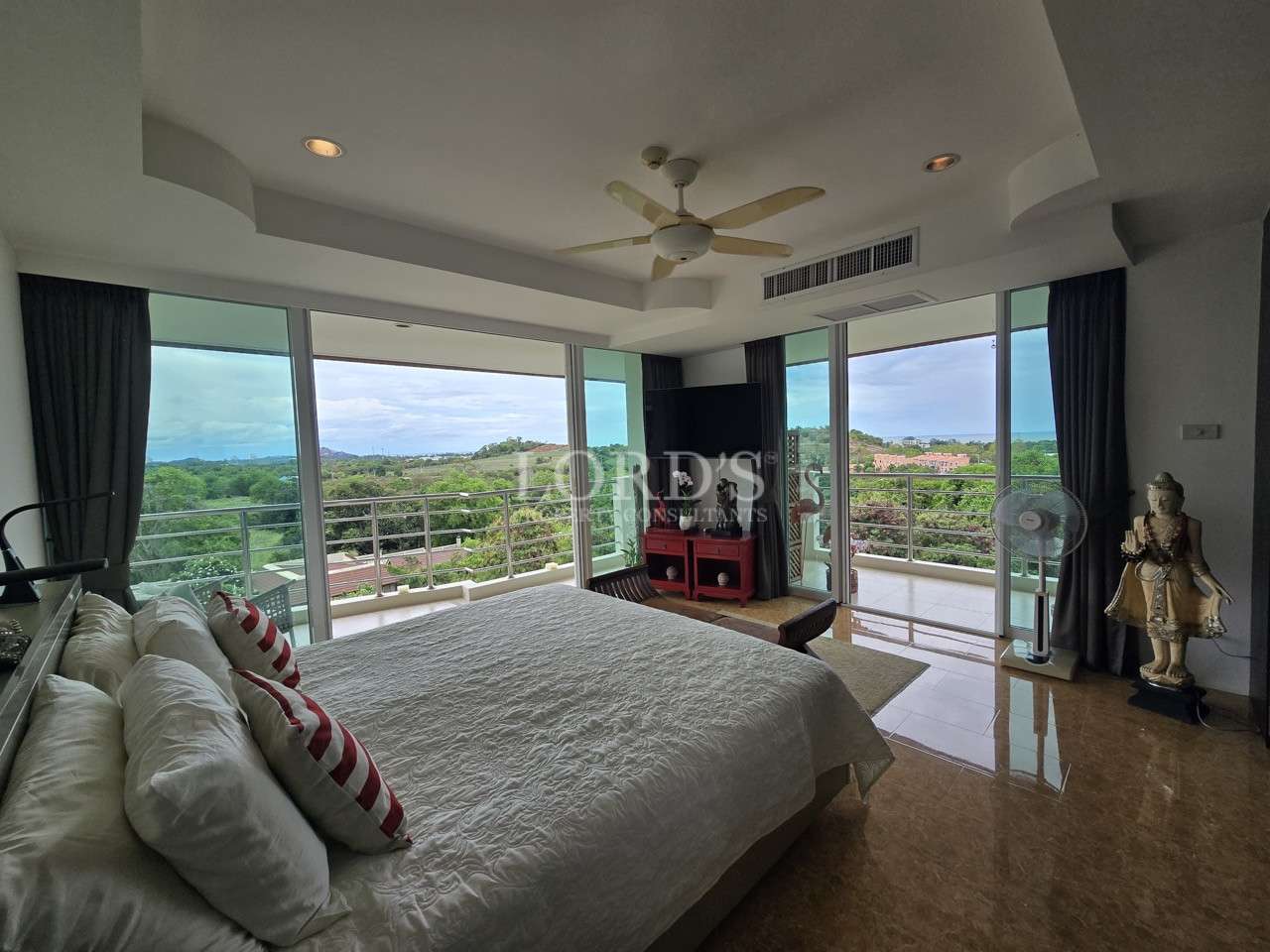 Master bedroom with large glass windows, balcony access, and panoramic views of hills and greenery.