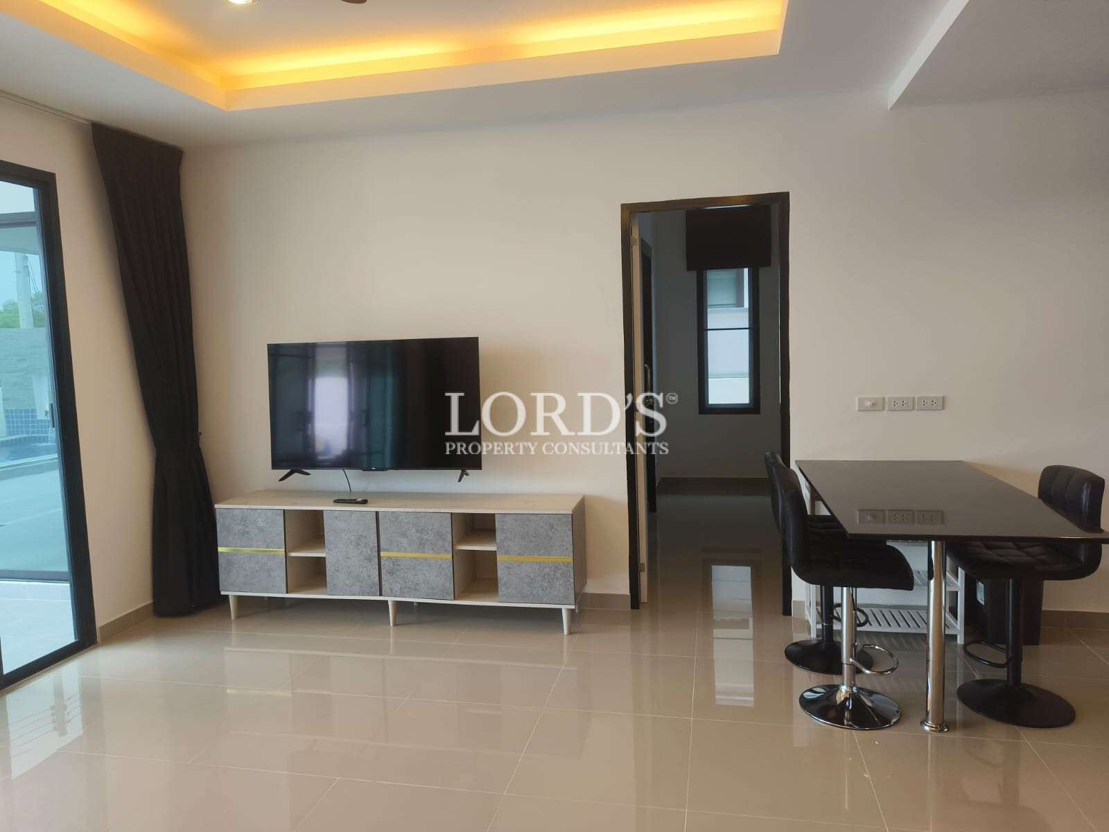 Modern living and dining area with flat-screen TV, media console, dining table with bar stools, and recessed ceiling lighting.