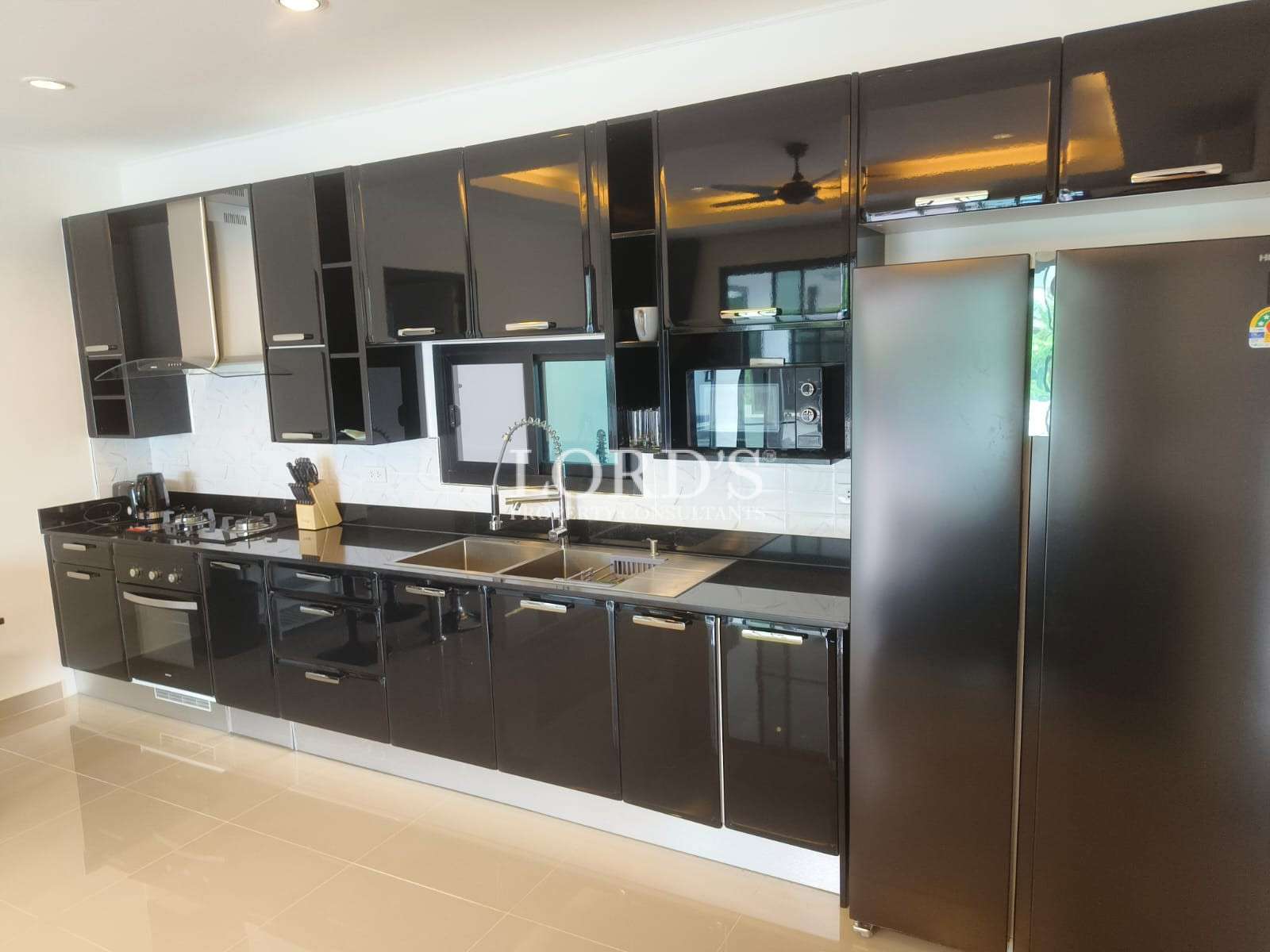 Modern kitchen with glossy black cabinets, built-in oven, sink, and large double-door refrigerator.