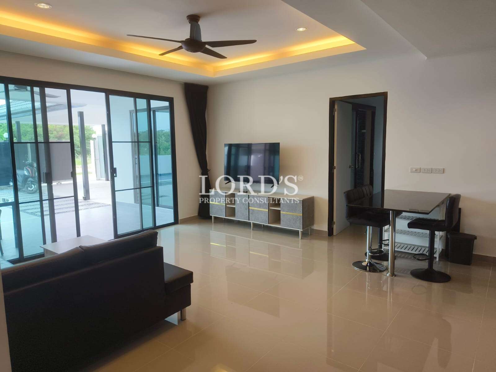 Modern open-plan living room with sofa, TV console, dining table, and sliding glass doors.