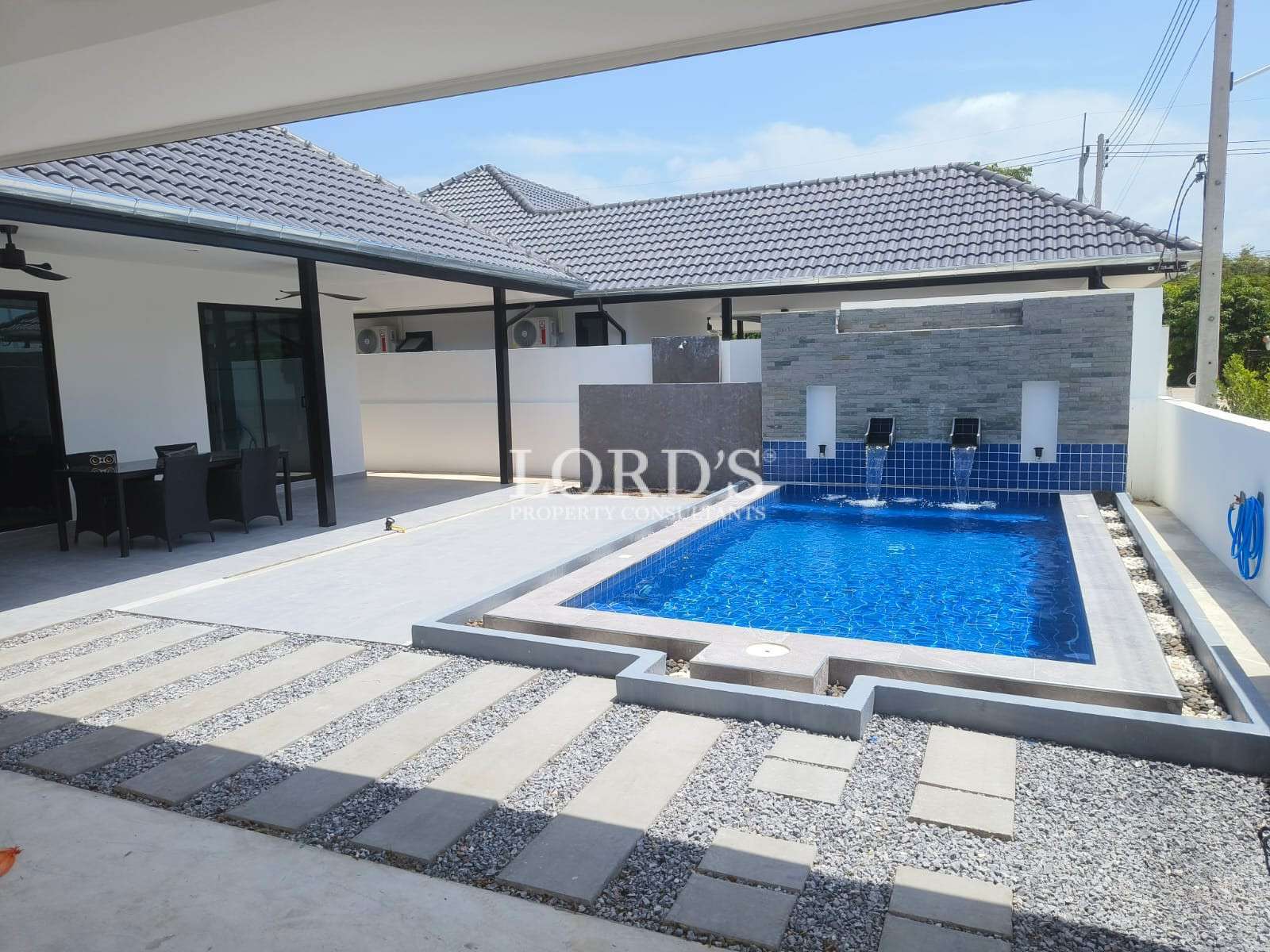 Modern villa courtyard with private swimming pool, tiled patio, and waterfall wall feature.