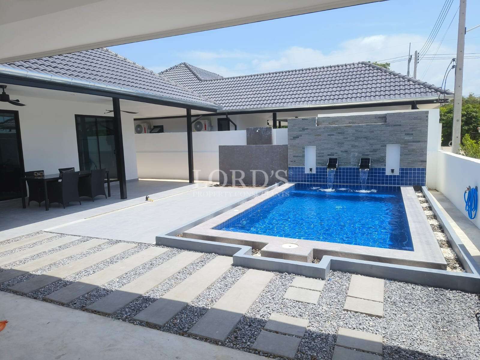 Modern courtyard with rectangular swimming pool, waterfall feature wall, and covered outdoor seating area.