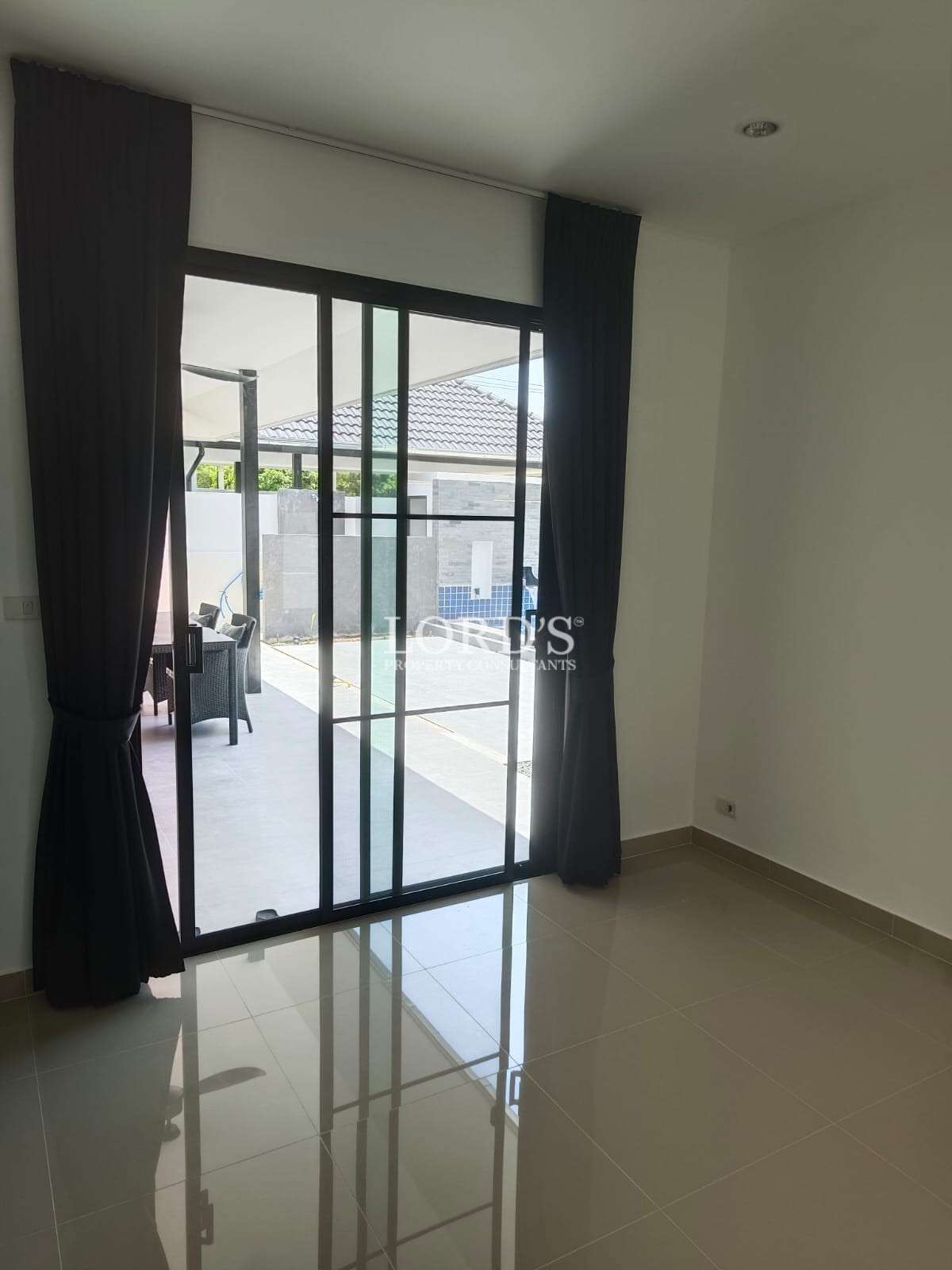 Empty modern room with glossy tiled floor and sliding glass door leading to a patio and pool area.