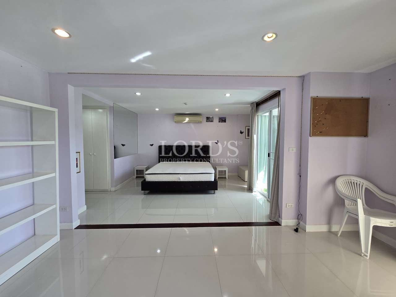 Large open bedroom with tiled flooring, shelving unit, and sliding glass doors.