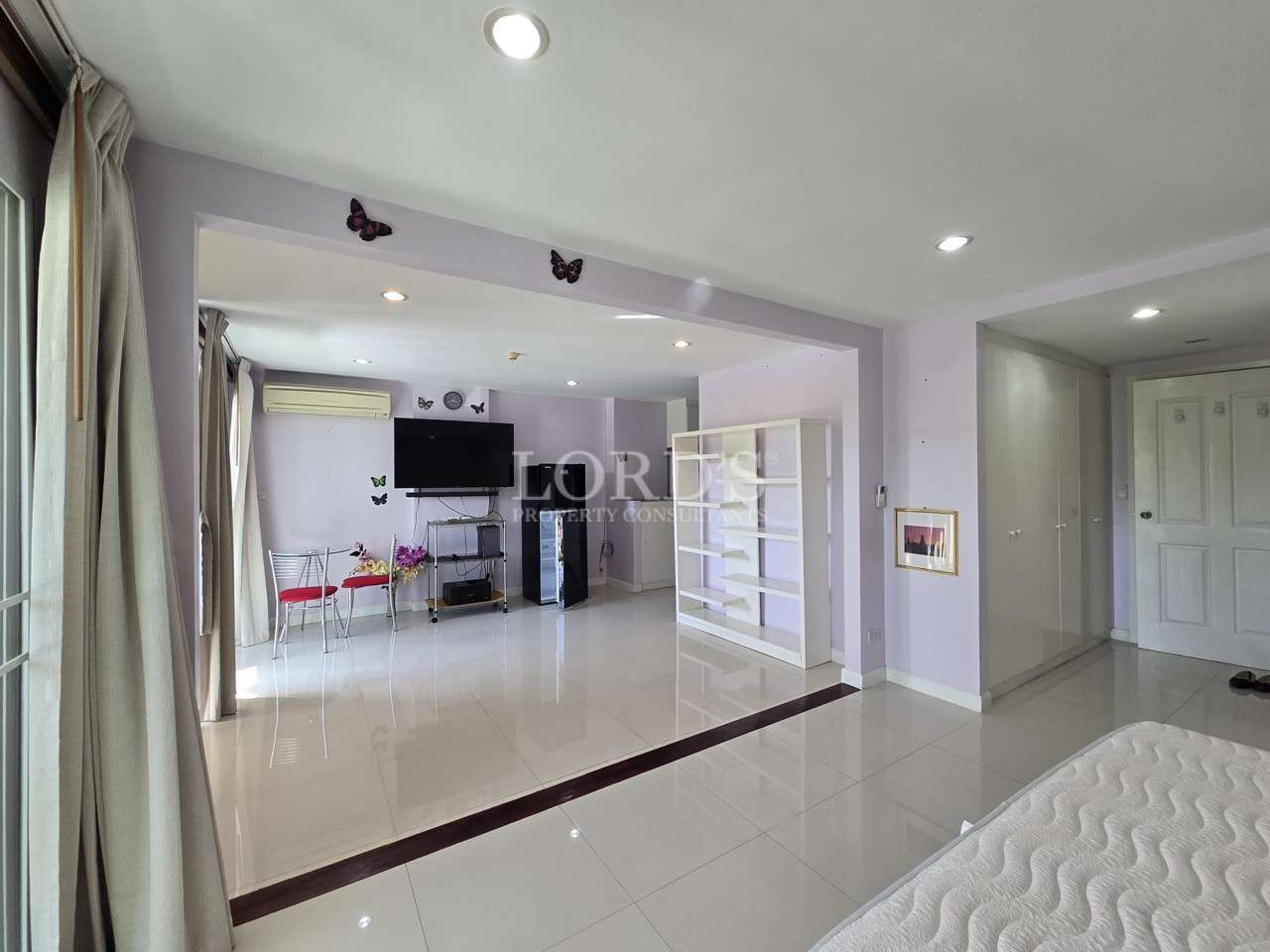 Large bedroom with open sitting area, TV, shelving, and tiled flooring.