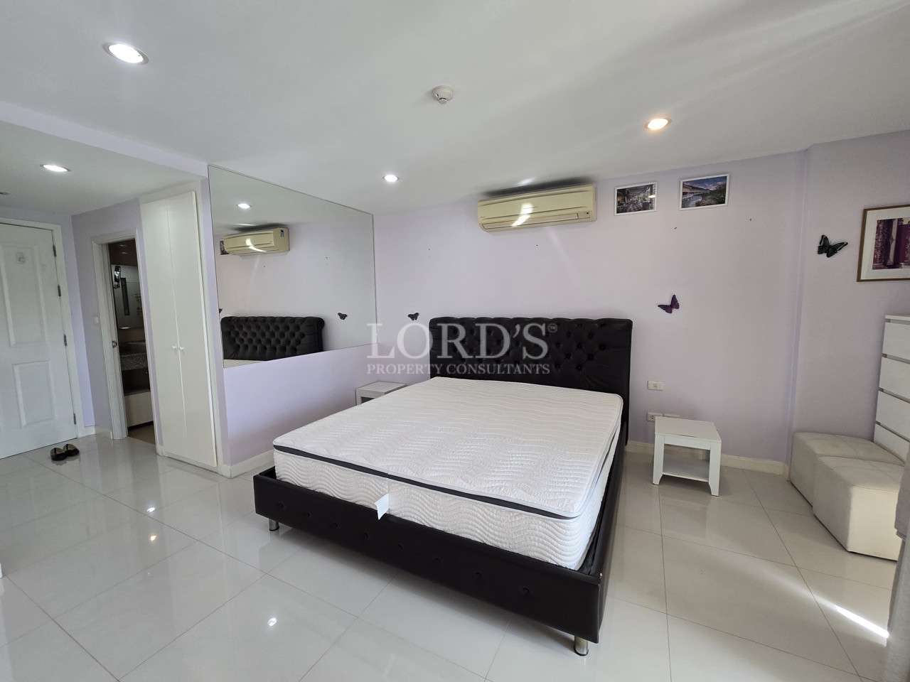 Bright bedroom with upholstered bed, mirrored wall, and air conditioning unit.