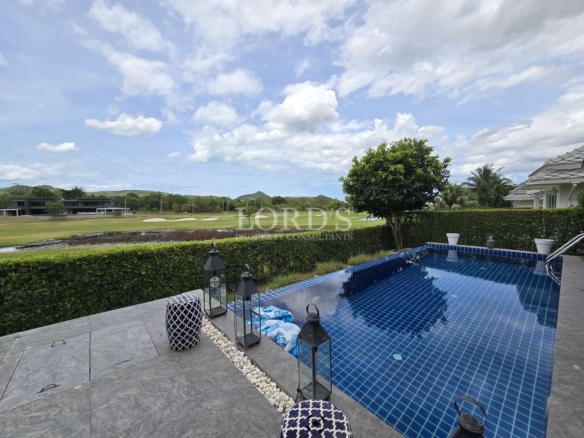 Private tiled swimming pool overlooking a golf course with green fairways, hedges, lantern decor, and a partly cloudy sky.