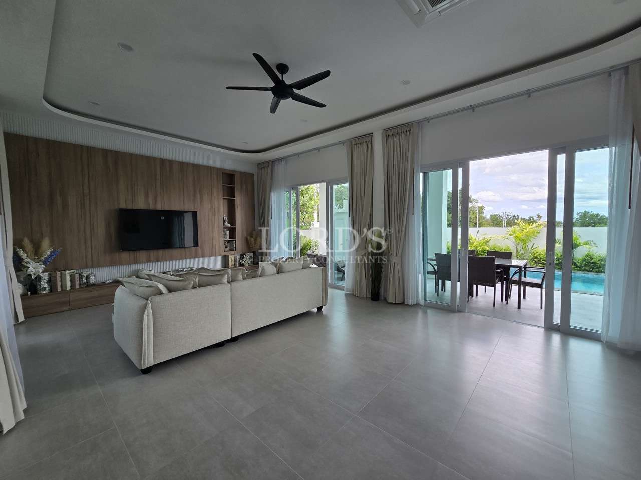 Spacious modern living room with beige sofa, wood feature wall, and sliding doors opening to a pool patio.