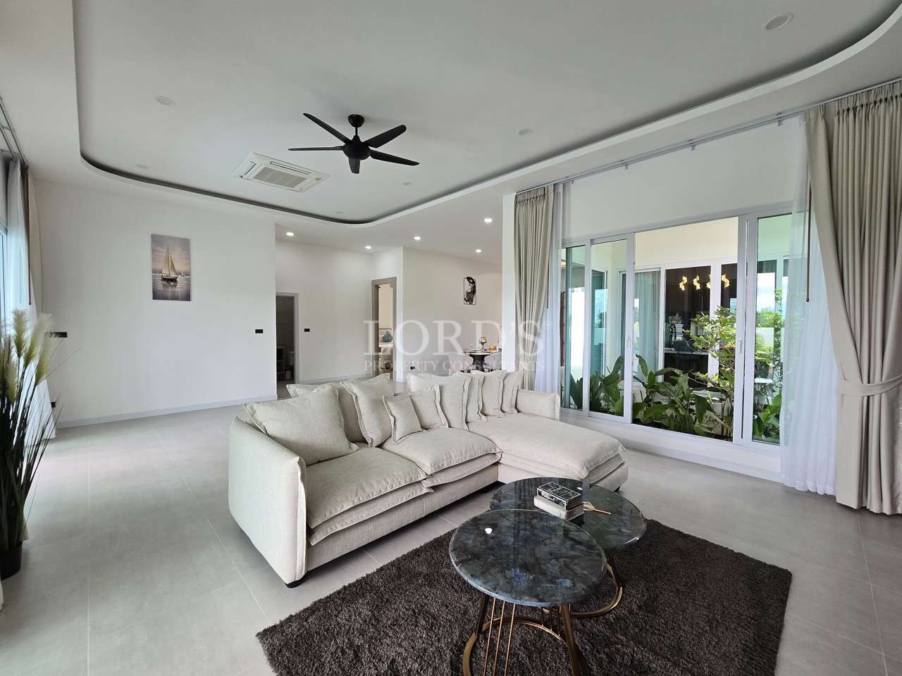 Modern living room with beige sectional sofa, marble coffee tables, and large sliding glass windows.