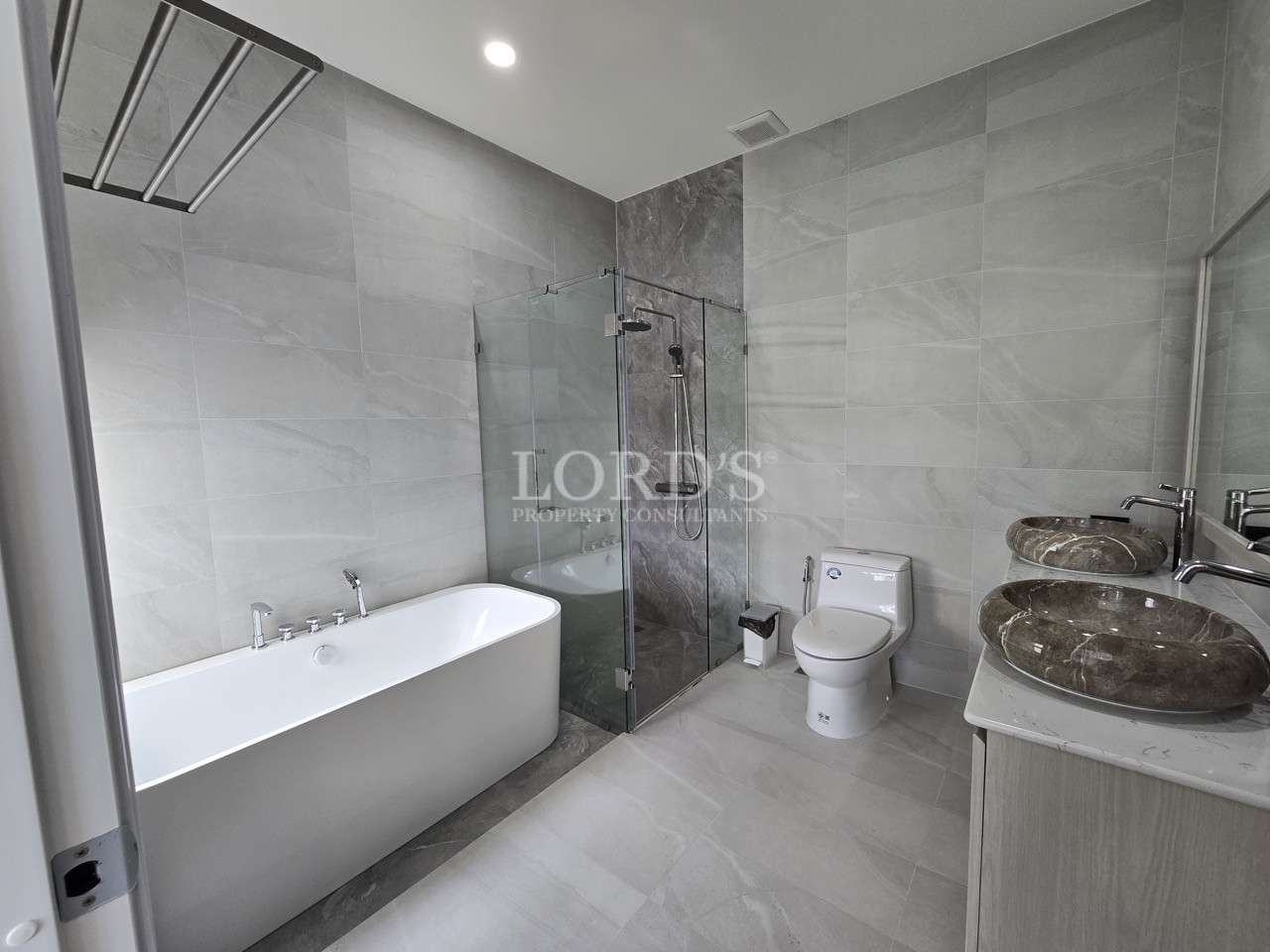 Modern gray-tiled bathroom with freestanding bathtub, glass shower enclosure, toilet, and double stone vessel sinks.