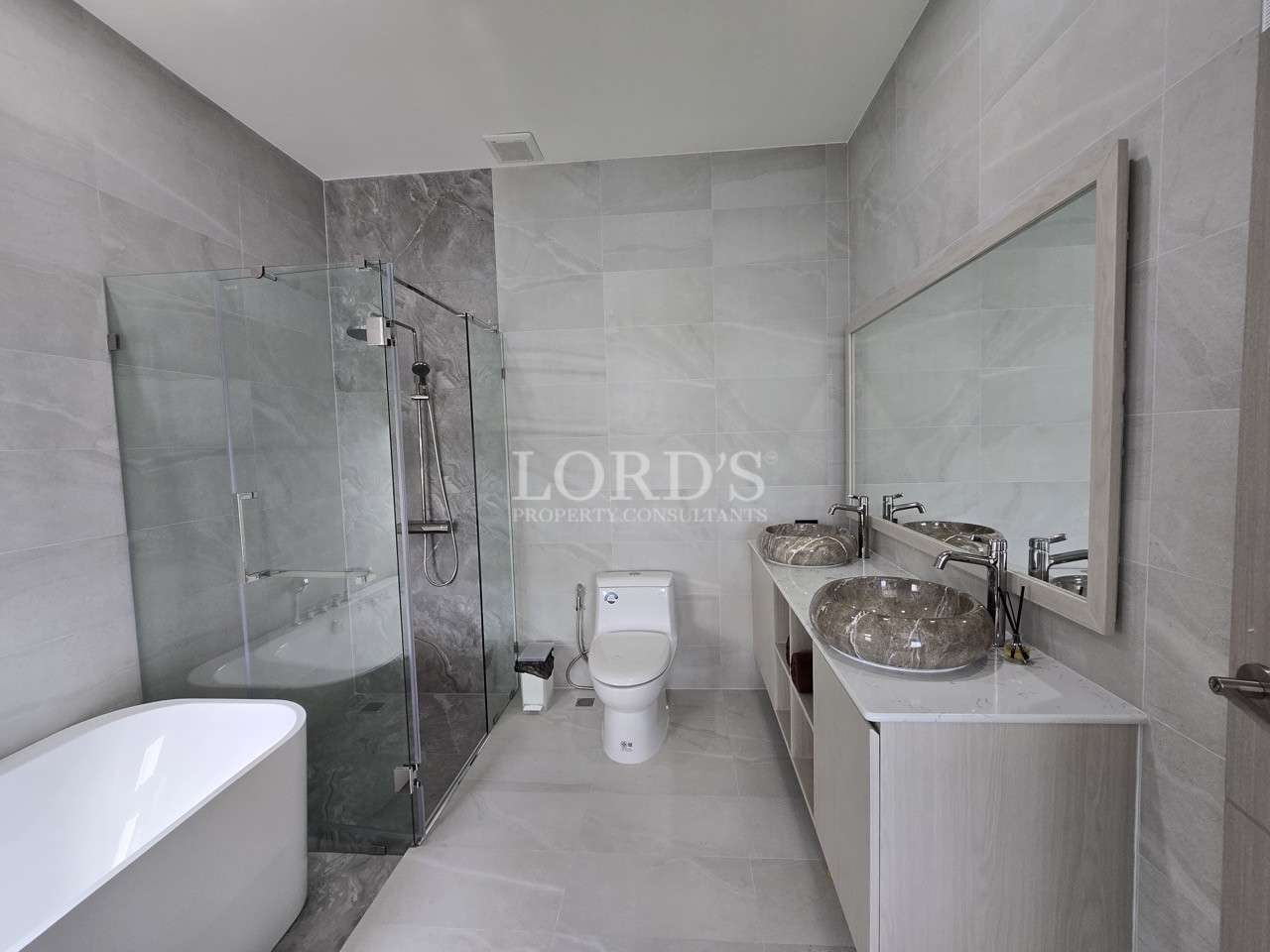 Modern bathroom with double stone vessel sinks, glass-enclosed shower, freestanding bathtub, and gray tile walls.