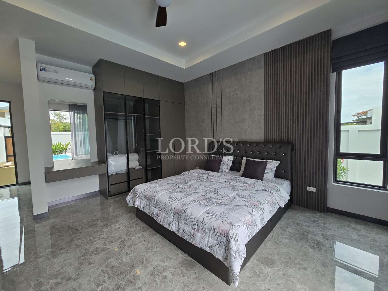 Modern bedroom with tufted headboard, built-in wardrobe, and marble flooring.