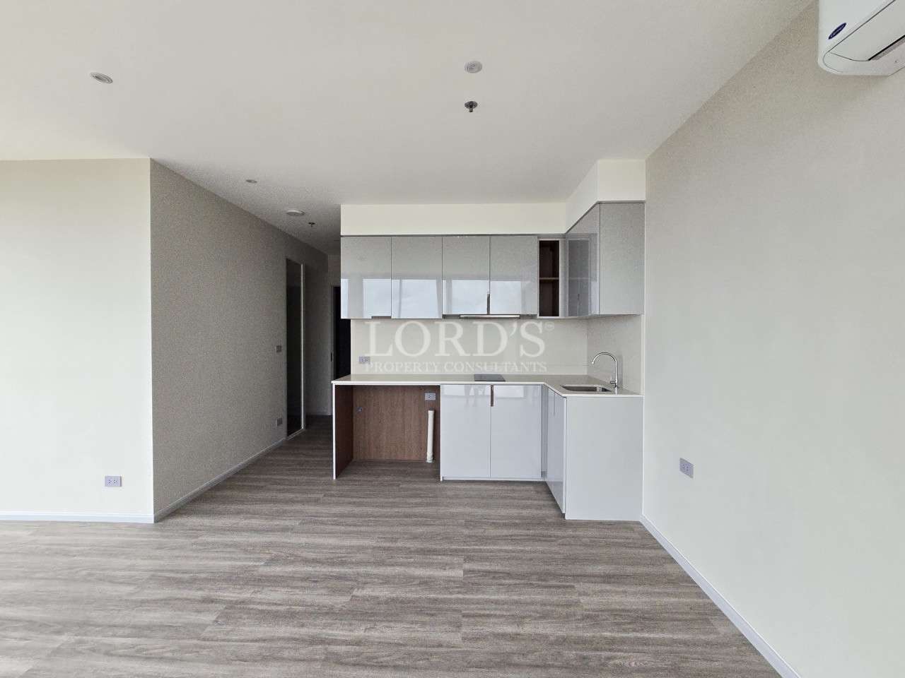 Modern studio apartment with compact kitchen, white cabinets, and wood-look flooring.