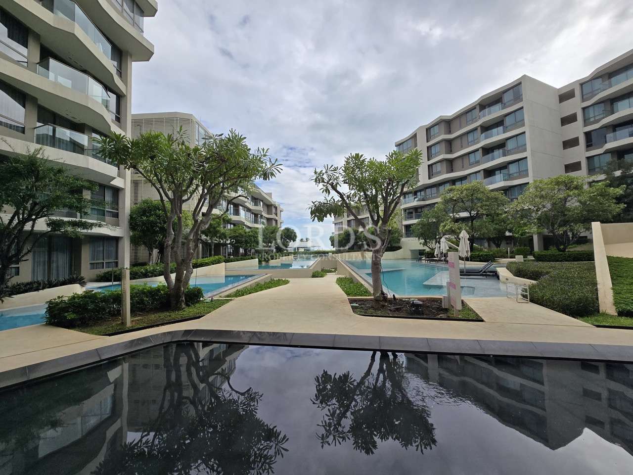 Luxury condominium complex with swimming pools, landscaped gardens, and modern buildings
