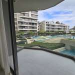 Condo balcony with glass railing overlooking swimming pool and landscaped garden