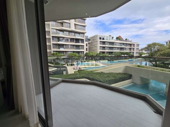 Condo balcony with glass railing overlooking swimming pool and landscaped garden