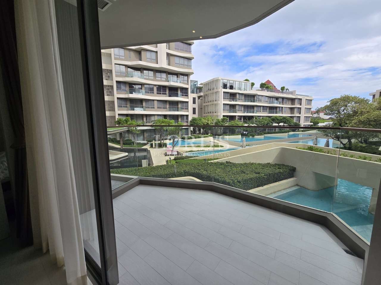 Condo balcony with glass railing overlooking swimming pool and landscaped garden